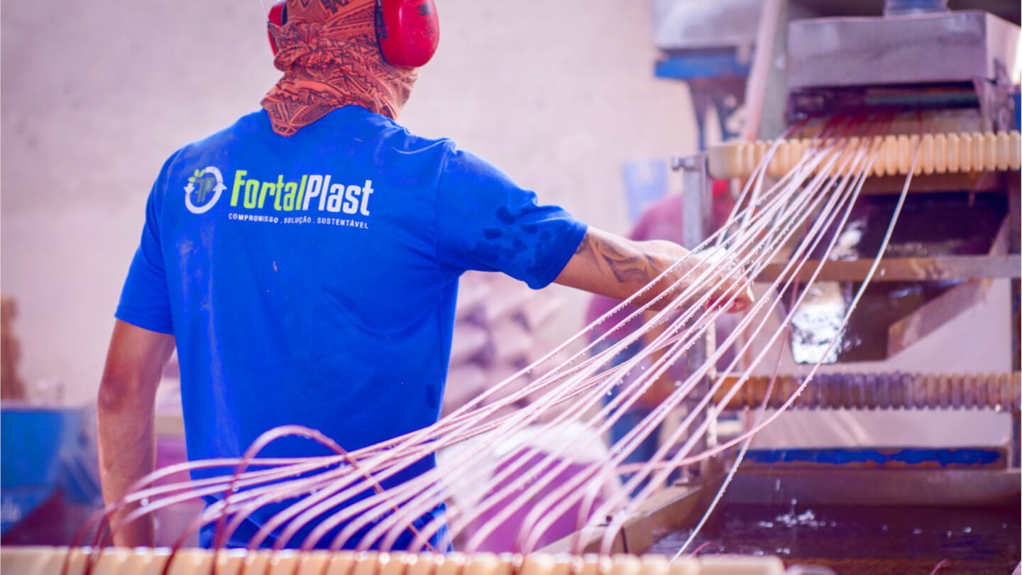 Homem ao lado da uma máquina com fios de plásticos